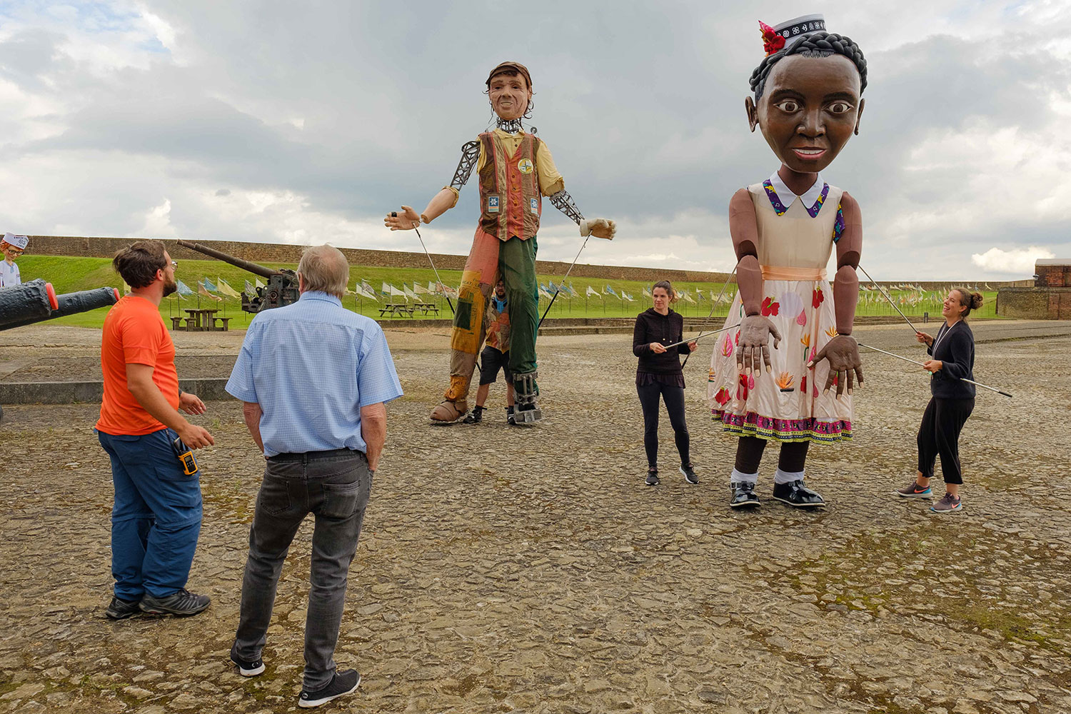 Two huge puppets stand facing the viewer, representing a Windrush girl and a Tilbury docker