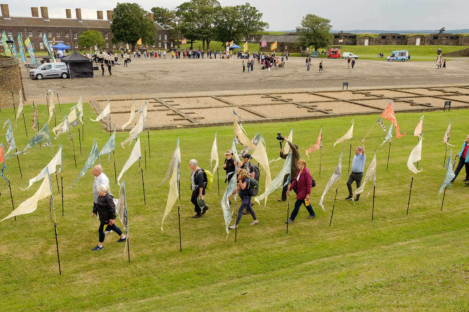 Wide shot of Tilbury Fort interior as a stream of walkers arrives through the Beach of Dreams flag installation