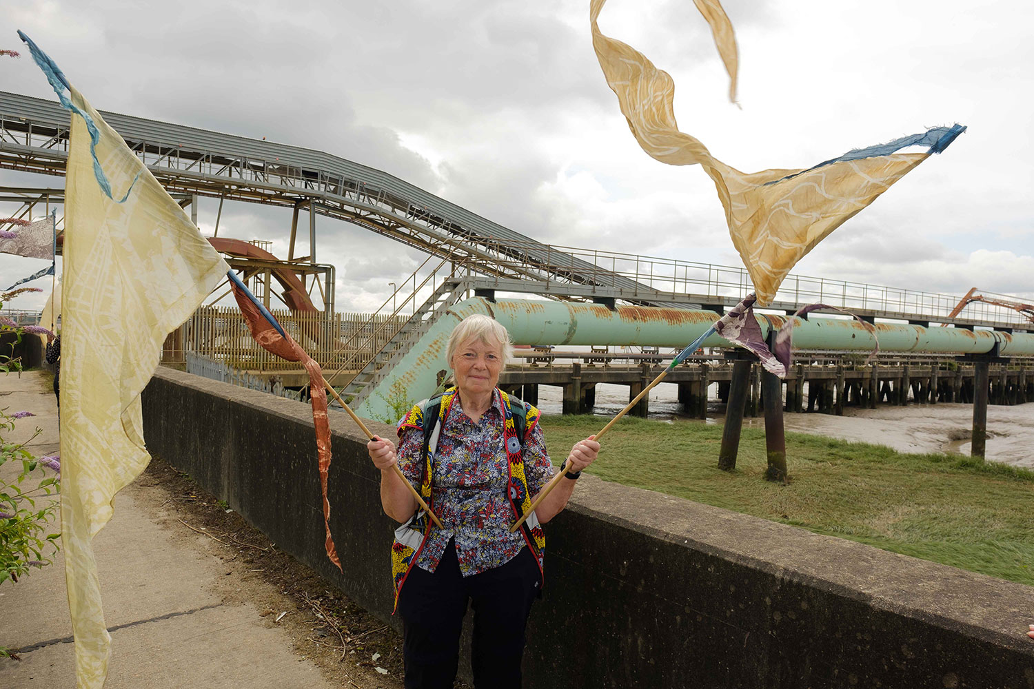 Lesley Robinson looks at the camera whilst holding silk pennants that illustrate the area