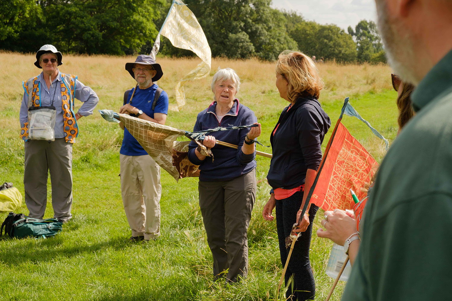Walkers gather in a group on grass holding silk pennants while Lesley talks about the dyes used to colour them
