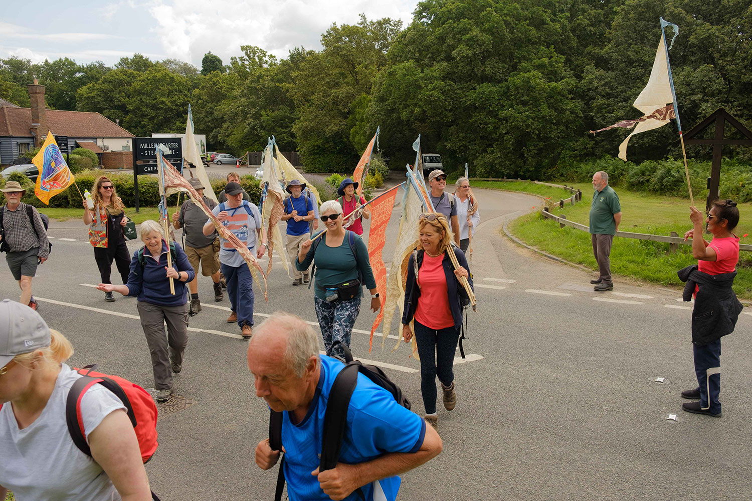 Group of walkers holding silk pennants walk towards the viewer crossing a road