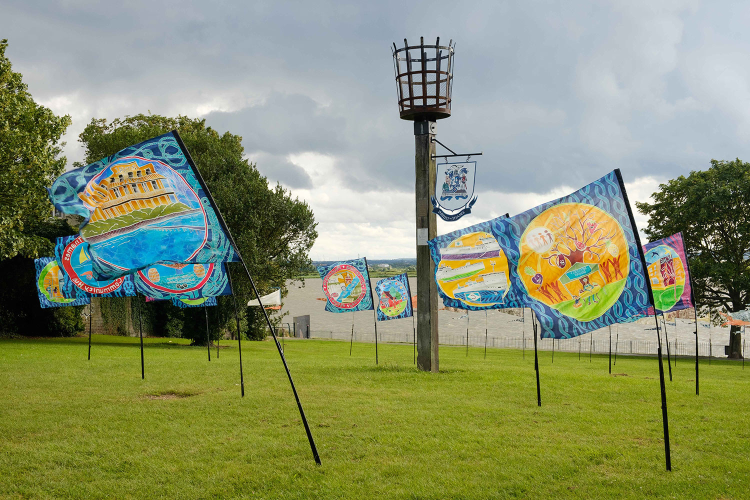 Flags illustrating aspects of the area decorate the grass in front of the Purfleet-on-Thames Beacon