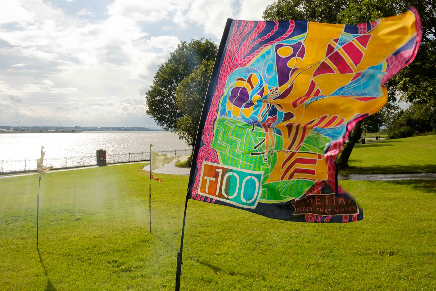An illlustrated T100 flag flutters in the breeze next to the river in Purfleet-on-Thames