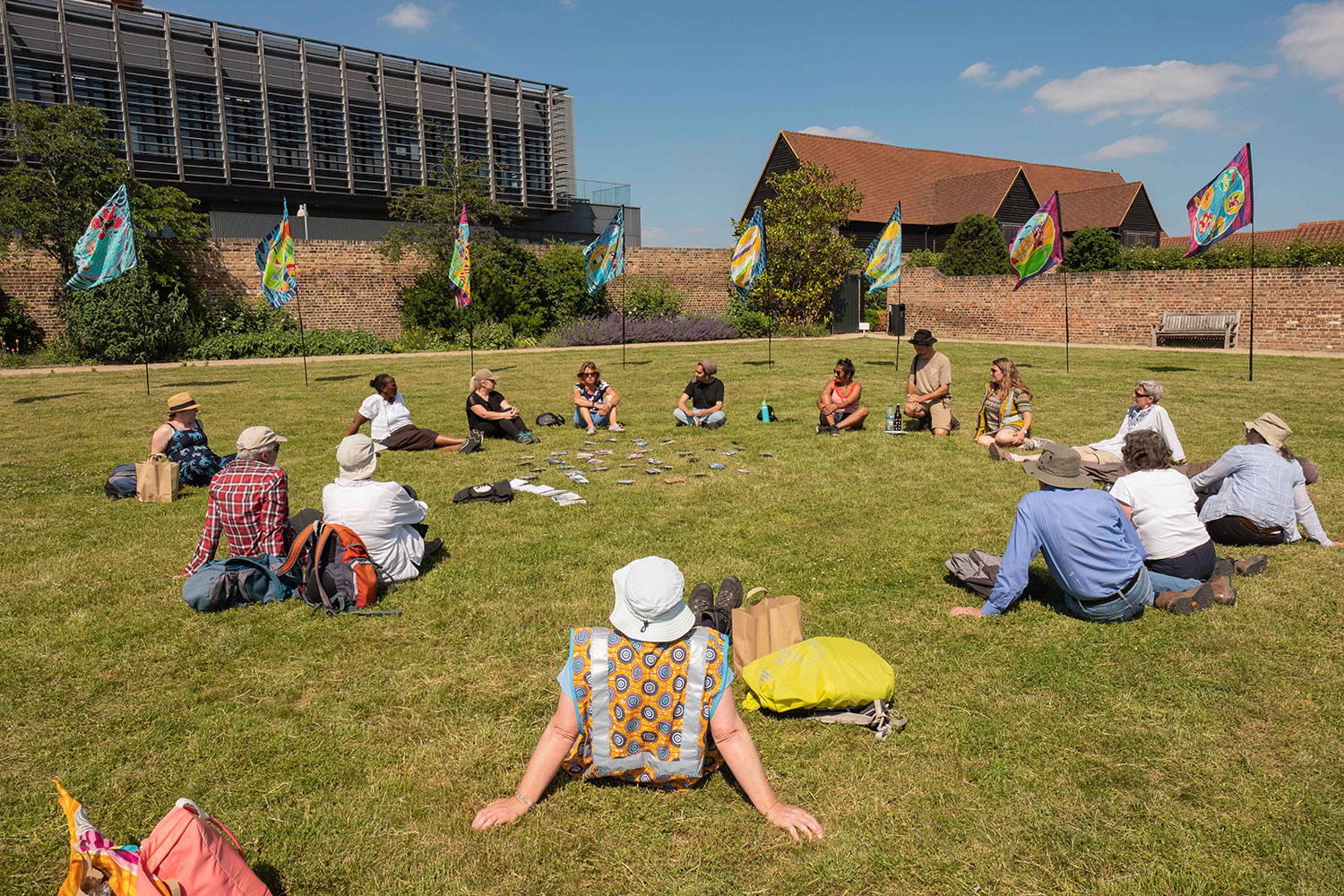 People sit in a circle on the grass at High House Production Park surrounded by flags